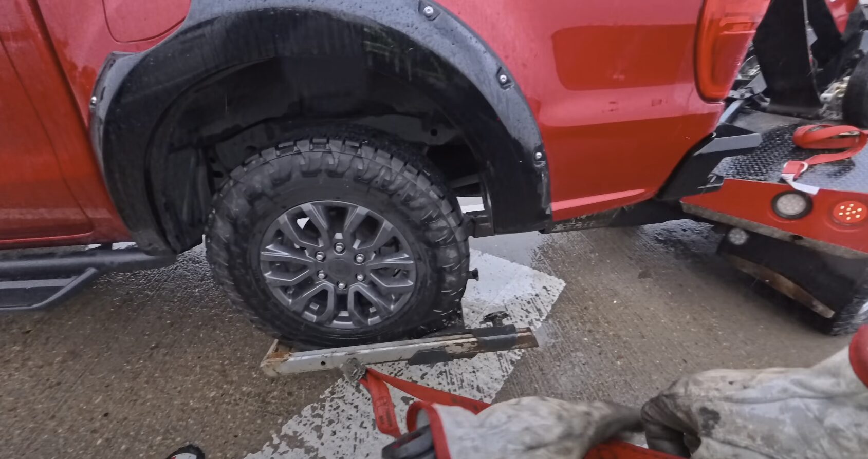 Red pickup truck being secured with chains on a professional tow truck